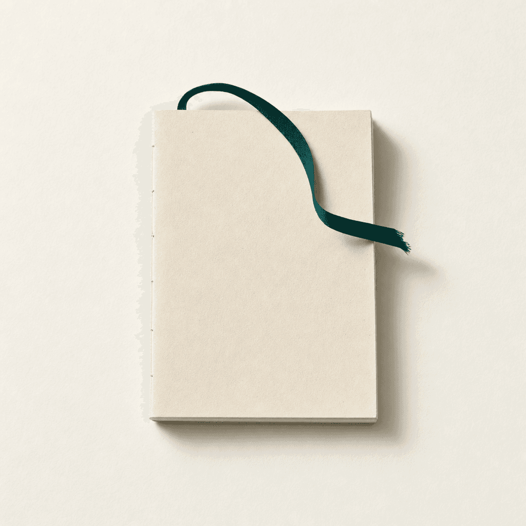 A small bound cream-paper notebook lying closed on a cream surface, with a thin deep-teal ribbon bookmark threading out from between its pages — kept private, not opened up.