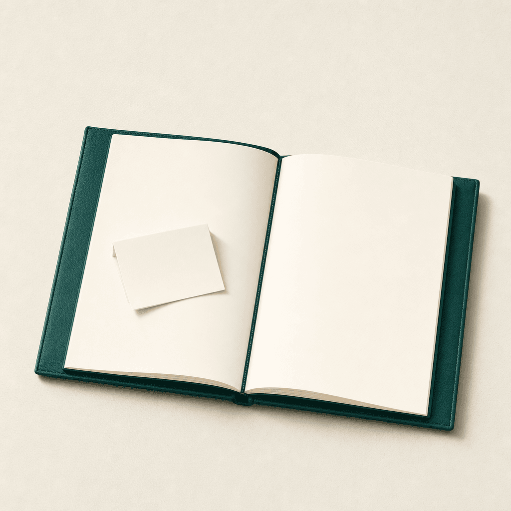 A large open leather-bound journal with a deep-teal cover lying flat on a cream surface, with a single cream-paper folded note resting on its open page — your note, into the journal you already keep.